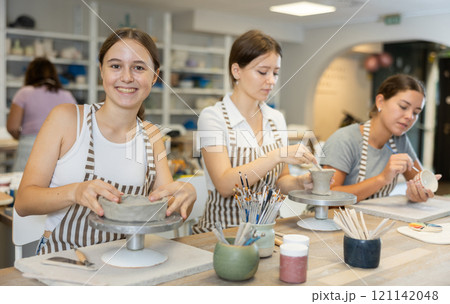 Three craftsperson are busy sculpting from clay and painting ceramic products 121142048