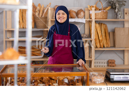 Asian Muslim woman bakery worker sells croissants, stand at counter and wait for visitors 121142062