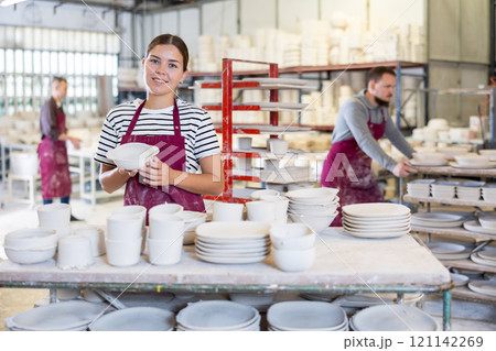 Smiling female artisan showcasing collection of ceramic plates in workshop Smiling female artisan showcasing collection of ceramic plates in workshop 121142269