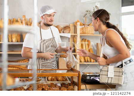 Salesman gives croissants to young girl in bakery Salesman gives croissants to young girl in bakery 121142274