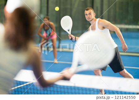 Girl paired with a man plays padel on an indoor tennis court 121142550