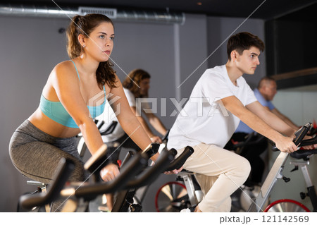 Man and woman taking indoor cycling class at fitness center, doing cardio riding bike 121142569
