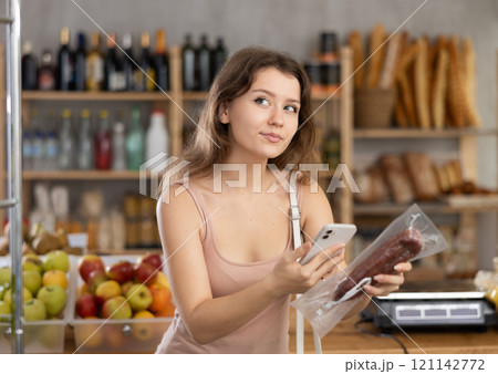 Young girl purchaser scanning QR code of dried sausage in supermarket Young girl purchaser scanning QR code of dried sausage in supermarket 121142772