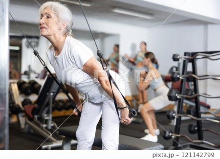 Mature woman working on special machine with ropes to develop arm muscles 121142799