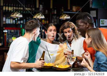 Cheerful multiracial soccer fans waving the flag of Ireland while drinking beer in the sport bar 121142819