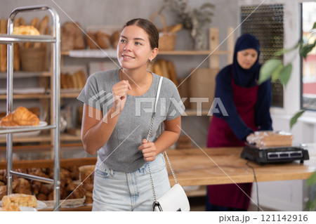 Young girl chooses some bakery goods while Muslim seller works in background in baker's Young girl chooses some bakery goods while Muslim seller works in background in baker's 121142916