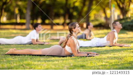 Yoga lesson visitors with coach perform dog face up and cobra pose in park Yoga lesson visitors with coach perform dog face up and cobra pose in park 121143315