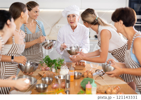 Elderly woman chef with bowl in hands tells women at culinary courses about traditions of cuisine Elderly woman chef with bowl in hands tells women at culinary courses about traditions of cuisine 121143331
