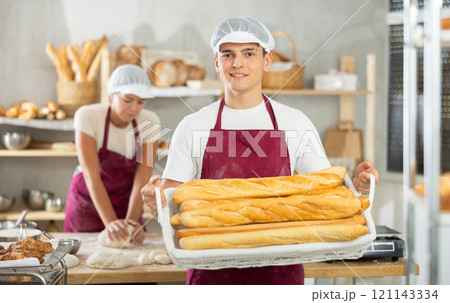 Young male baker holding baguettes in wicker basket 121143334