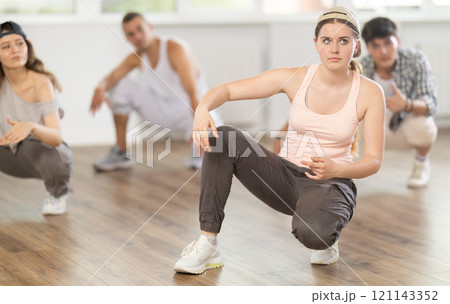 Young girl performing sitting pose of breakdance in training hall Young girl performing sitting pose of breakdance in training hall 121143352