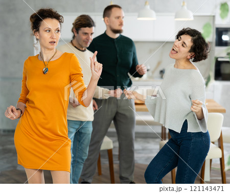 Four adult friends dancing and singing at home. Cheerful women and men enjoy music together. Happy people celebrating friendship 121143471