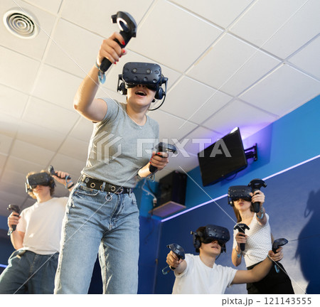 Girl is enjoying exciting movie with friends in VR glasses in room Girl is enjoying exciting movie with friends in VR glasses in room 121143555