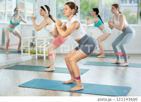 Young woman during Pilates strength training performs squats with elastic band on legs and shins Young woman during Pilates strength training performs squats with elastic band on legs and shins 121143600