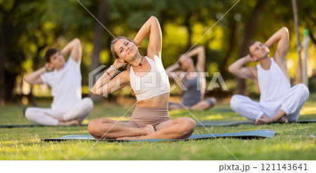 Girl performing stretches in lotus position during group yoga outdoors 121143641