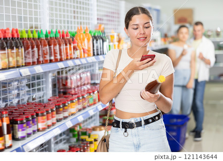 Girl reads a QR code from a bottle of hot sauce in chinese supermarket. Girl reads a QR code from a bottle of hot sauce in chinese supermarket. 121143644