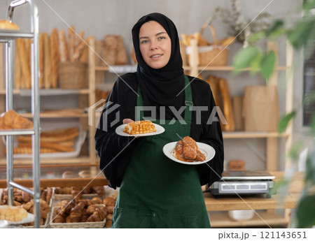 Young Muslim woman bakery owner offering fresh pastries 121143651