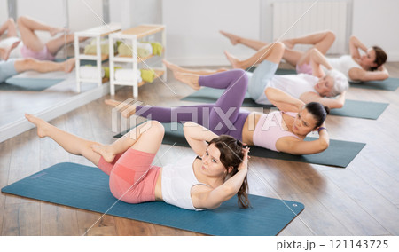 Girl doing bicycle crunches during group pilates training Girl doing bicycle crunches during group pilates training 121143725