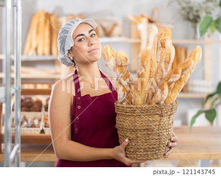 Young saleswoman displays baguettes in wicker basket Young saleswoman displays baguettes in wicker basket 121143745