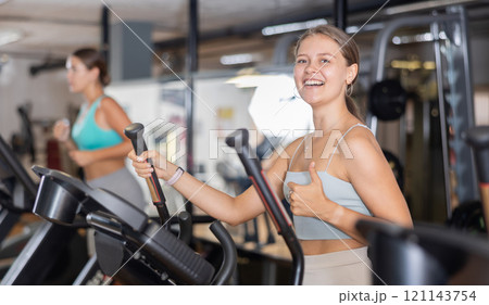 Portrait of sporty woman doing cardio workout on elliptical cross trainer at fitness center Portrait of sporty woman doing cardio workout on elliptical cross trainer at fitness center 121143754