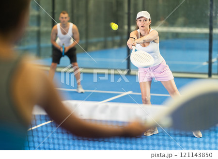 Woman with racket training on indoor court playing padel game and hitting ball Woman with racket training on indoor court playing padel game and hitting ball 121143850