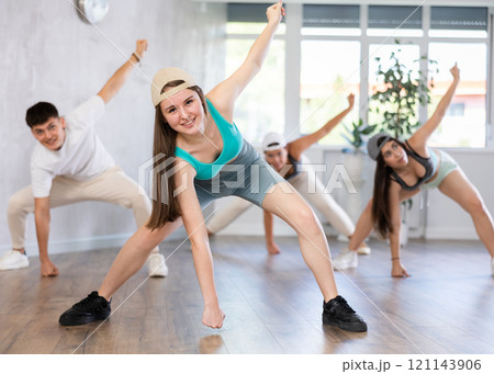 Young girl in ball cap and teenagers actively move and dance hip hop at choreography lesson Young girl in ball cap and teenagers actively move and dance hip hop at choreography lesson 121143906