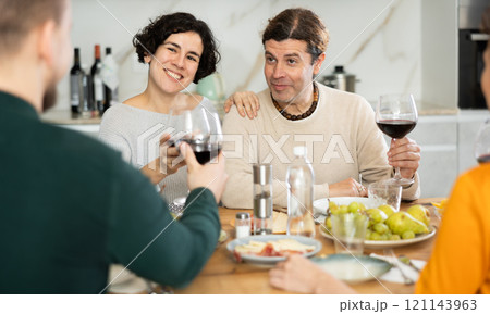 Group of joyful individuals are celebrating a holiday, enjoying drinks and conversation around table in their home Group of joyful individuals are celebrating a holiday, enjoying drinks and conversation around table in their home 121143963