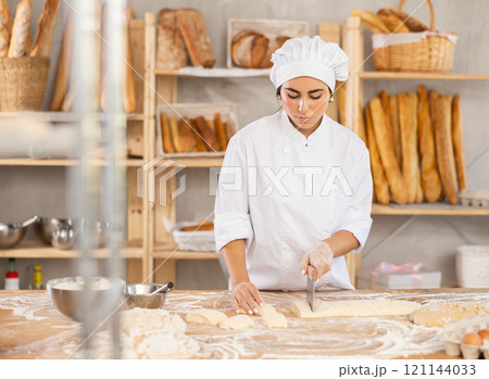 Young female baker cutting dough with scraper Young female baker cutting dough with scraper 121144033