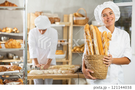 Young woman are standing in kitchen with basket of finished products baguettes Young woman are standing in kitchen with basket of finished products baguettes 121144038
