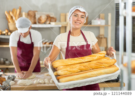 Young woman are standing in kitchen with basket of finished products baguettes Young woman are standing in kitchen with basket of finished products baguettes 121144089