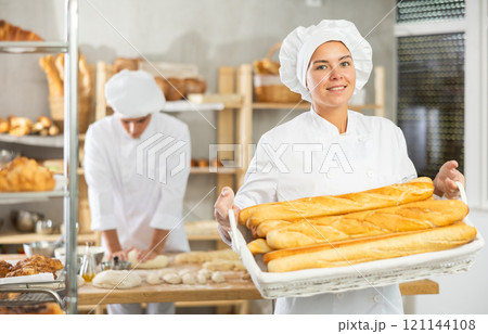 Happy female baker posing with basket of freshly baked baguettes in bakery, demonstrating concept of food industry and baker profession Happy female baker posing with basket of freshly baked baguettes in bakery, demonstrating concept of food industry and baker profession 121144108