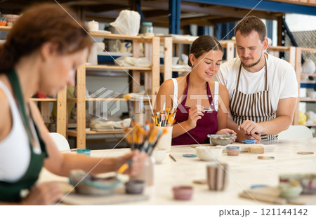Male pottery teacher helps students shape clay into plates and dishes 121144142
