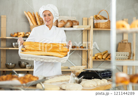Smiling female baker presenting fresh baguettes in bakery 121144289