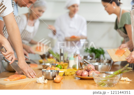 Pleased young man learner of culinary classes cutting piece of salmon Pleased young man learner of culinary classes cutting piece of salmon 121144351