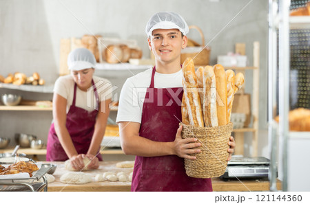 Enthusiastic young baker presenting freshly baked golden baguettes Enthusiastic young baker presenting freshly baked golden baguettes 121144360