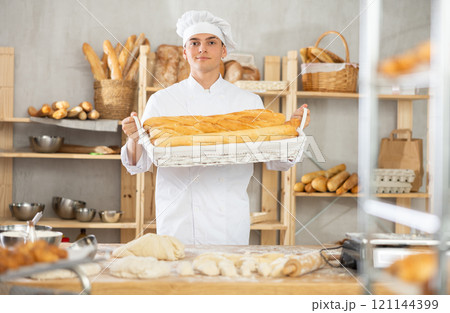 Young male baker holding baguettes in wicker basket 121144399