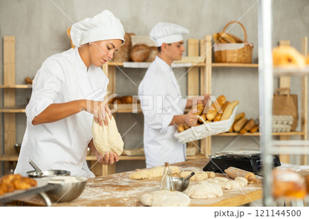 Young woman works in bakery as baker, kneads and prepare dough, works with flour. 121144500
