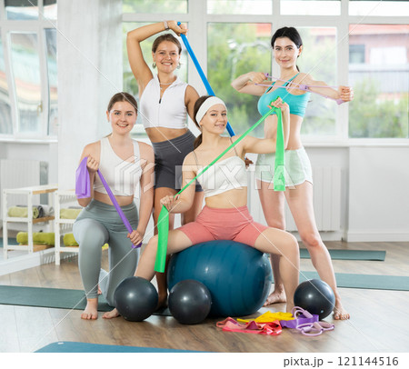 Young men and women posing together in training room holding resistance bands 121144516
