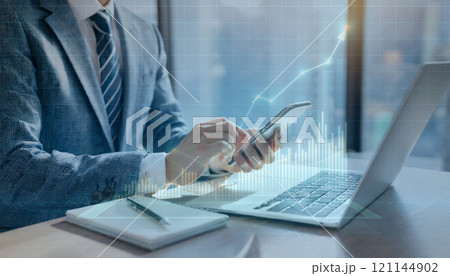 パソコンとスマホを操作するスーツを着た男性。高層階のオフィス。 121144902
