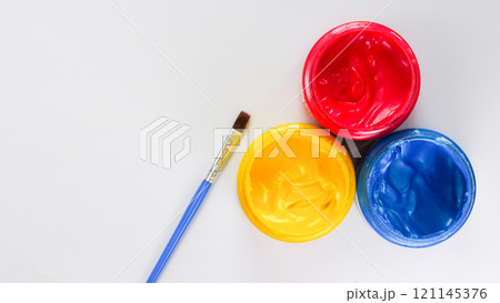 Three jars of red, yellow, and blue paint with a blue-handled brush on a white background. Perfect for art and creativity themes. 121145376