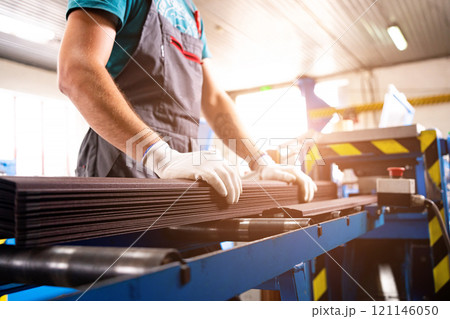 A factory worker is making a metal profile for a roof. Worker at factory measures metal profiled sheet. He works in metal production industrial. metal roofing production, production of roof elements 121146050