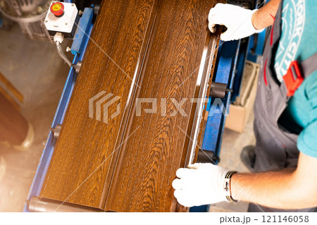 A factory worker is making a metal profile for a roof. Worker at factory measures metal profiled sheet. He works in metal production industrial. metal roofing production, production of roof elements A factory worker is making a metal profile for a roof. Worker at factory measures metal profiled sheet. He works in metal production industrial. metal roofing production, production of roof elements 121146058