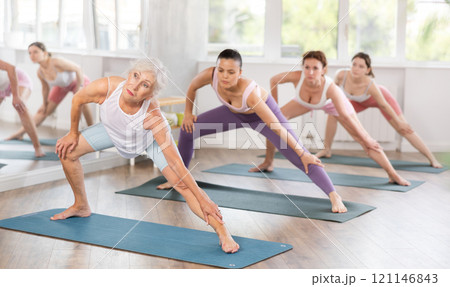 Senior lady performing Side Lunge Pose during group training 121146843