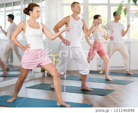 Young men and women doing shoulder workout with resistance band in standing positions 121146898