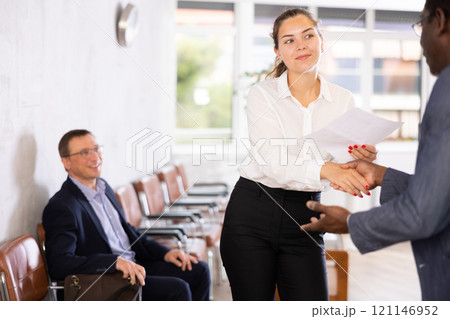 Young woman handshaking with other person in waiting room Young woman handshaking with other person in waiting room 121146952