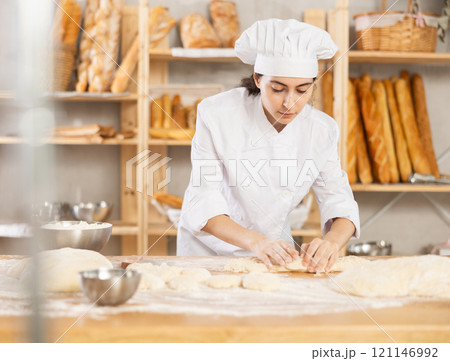 Young female baker kneading dough on table 121146992