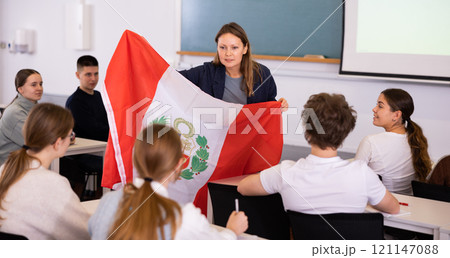 Teenage students in class and listening carefully to female teacher holding Peru flag in hands 121147088