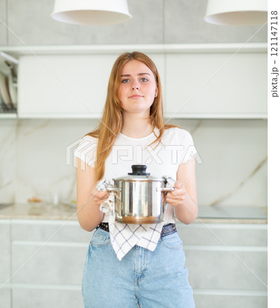 Portrait of teen girl holding small pot in her hands after cooking in cozy kitchen Portrait of teen girl holding small pot in her hands after cooking in cozy kitchen 121147118