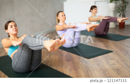 Focused active women balaning in sitting boat posture Paripurna Navasana while training together in yoga center 121147131