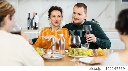 Two married couples are sitting at table, enjoying food and wine, chatting, talking, laughing. 121147269