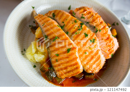 Tasty steak of grilled salmon in sauce with pepper and lemon on plate Tasty steak of grilled salmon in sauce with pepper and lemon on plate 121147492